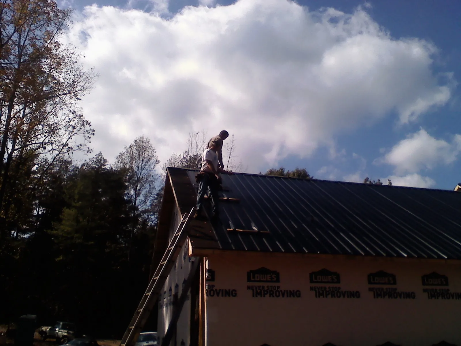 Roofer fastening dark metal panels high against a cloudy sky, from a Roof Inspection job in Newark