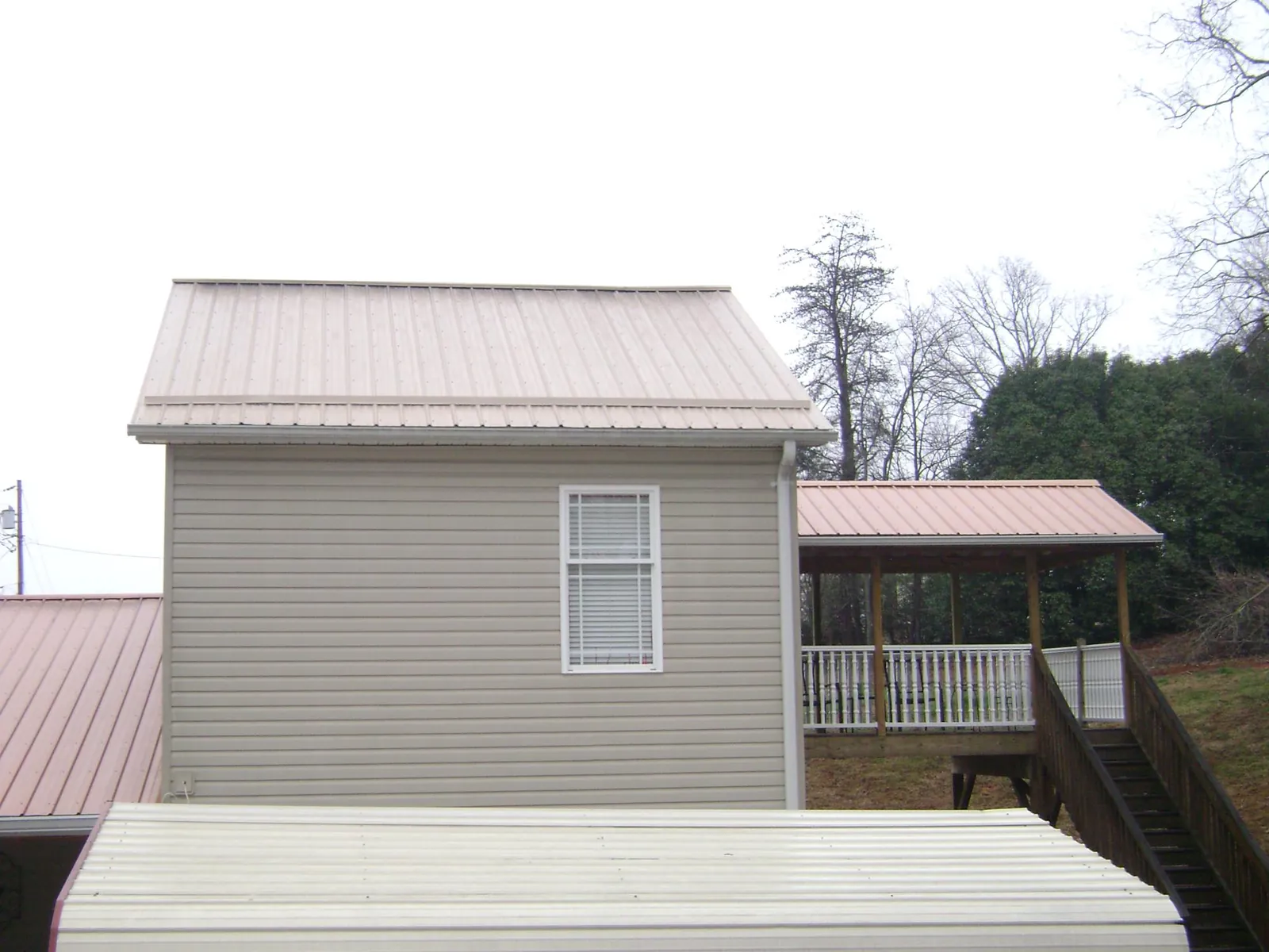Tan metal roofs on a two story addition and attached porch, from a Roof Replacement job in Newark